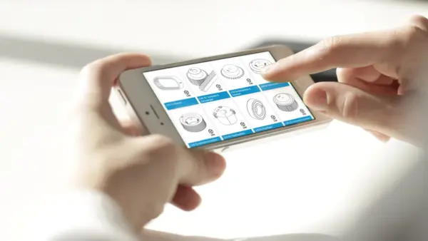 Zwei Hände halten ein Smartphone, auf dessen Display der Z24-Onlineshop mit technischen CAD-Zeichnungen von Zahnrädern und Antriebselementen zu sehen sind.