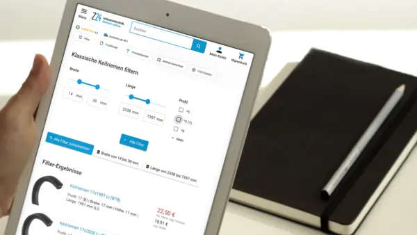Hand hält ein Tablet mit geöffneter Z24-Webseite, auf der ein Filter für klassische Keilriemen angezeigt wird; daneben liegen ein Notizbuch und ein Stift.