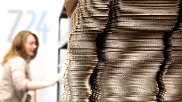 Mitarbeiterin der Z24 GmbH im Lager neben einem großen Stapel Versandkartons aus Wellpappe.