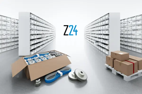 Modernes Lager mit hohen Regalen auf beiden Seiten, gefüllt mit vielen kleinen Verpackungen. In der Mitte stehen geöffnete Kartons mit blauen Zahnriemen und Verpackungsmaterial auf dem Boden. Im Hintergrund ist das Z24-Logo zu sehen